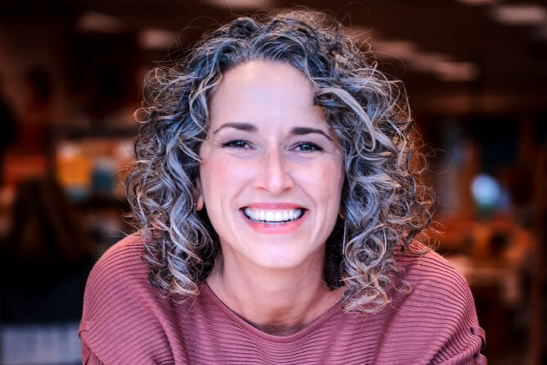 A woman smiles as she leans against a table.