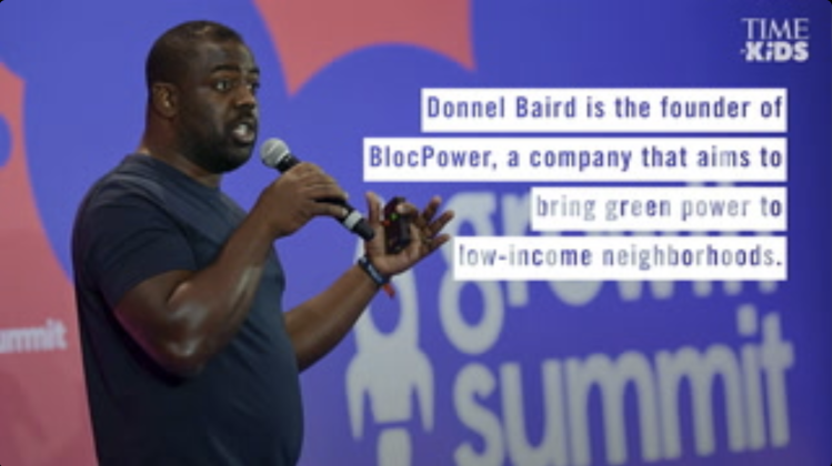Man, Donnel Baird, speaking into a microphone at a summit in front of a backdrop with the text overlay that reads: Donnel Baird is the founder of BlocPower, a company that aims to bring green power to low-income neighborhoods. 