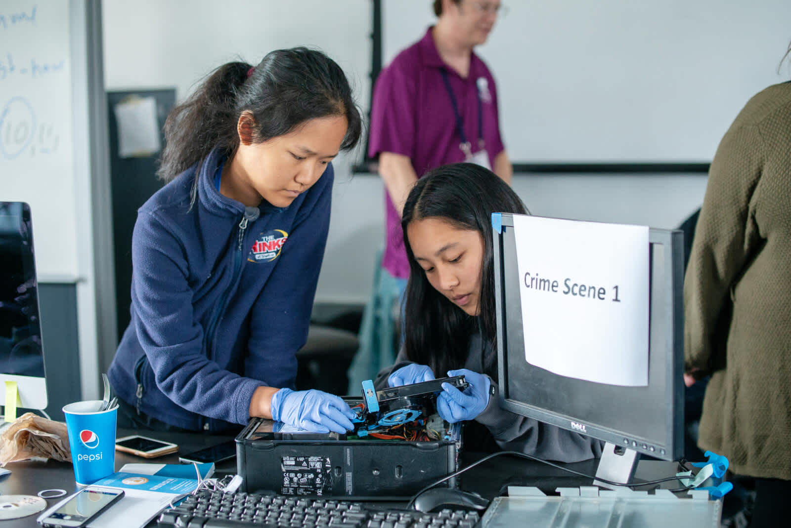 Two students examining the inside of a computer next to a monitor with a sign that says, "Crime Scene 1"