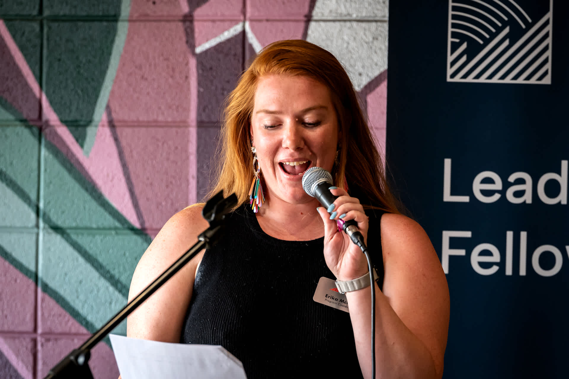 A woman speaks into a microphone as she reads from a sheet of paper.