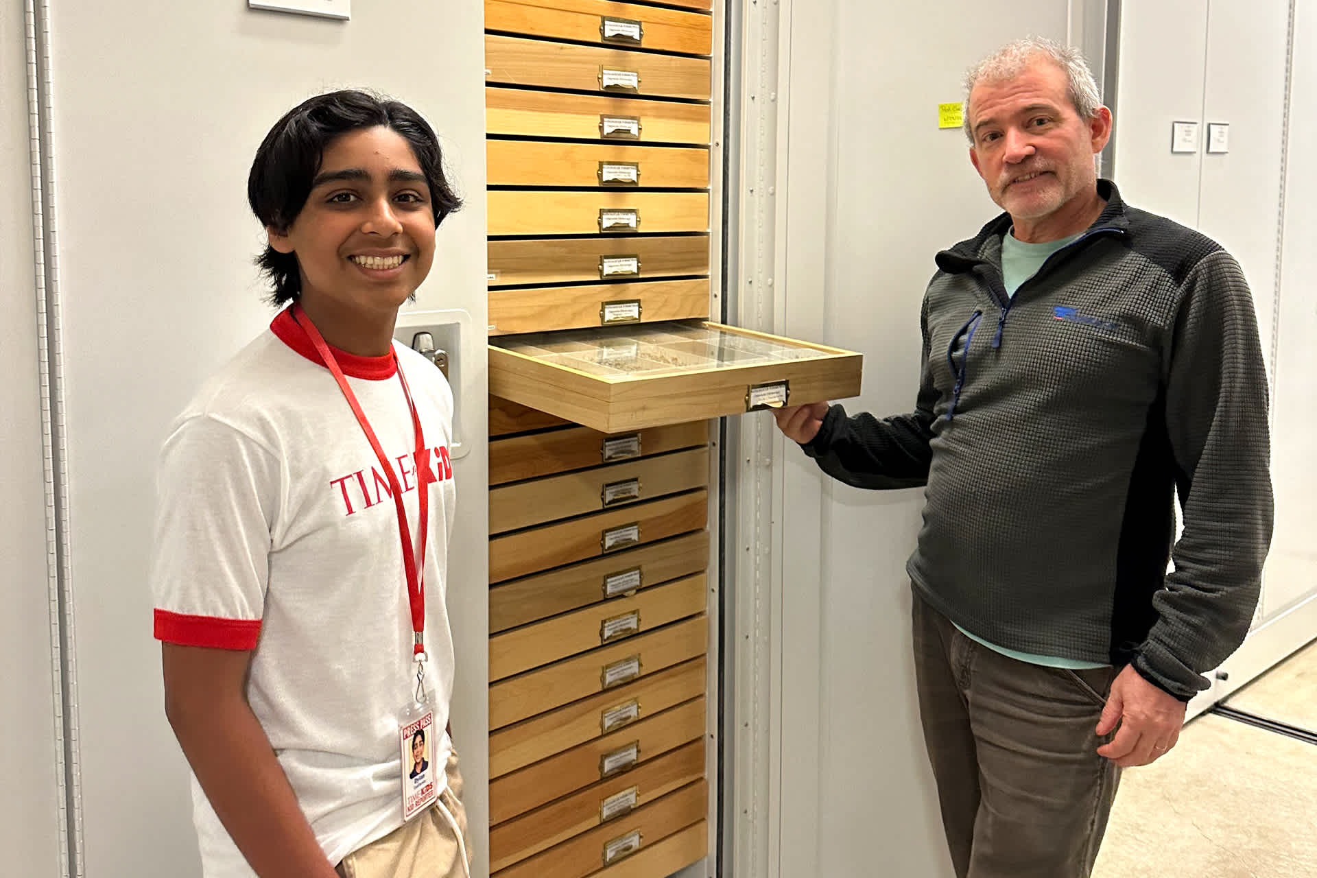 A boy and a man standing near a cabinet of drawers, smiling.