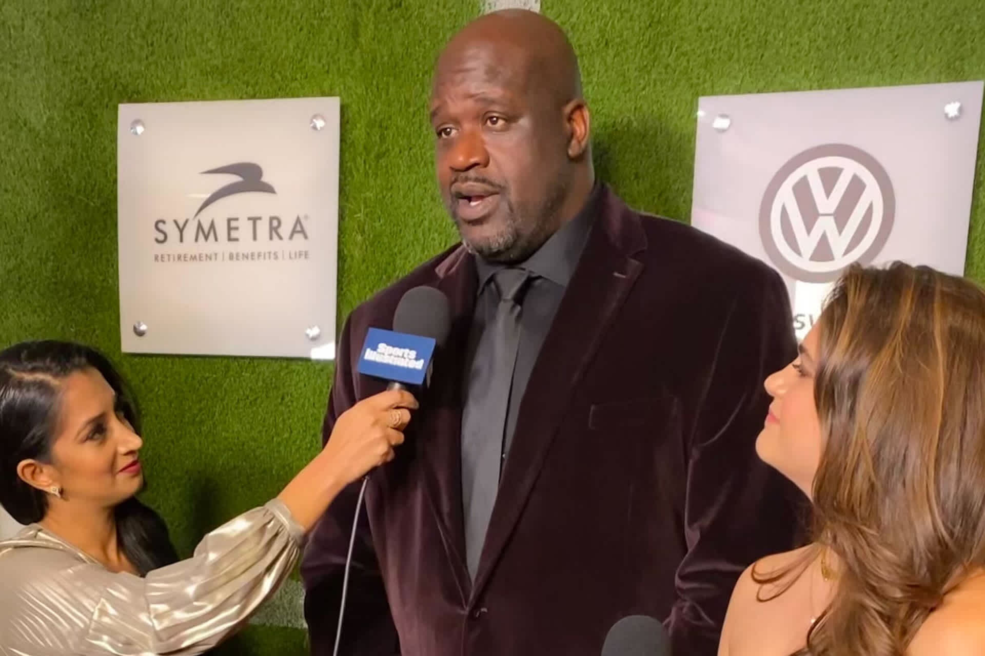 Desai, in gold dress, holds a microphone up to Shaquille O'Neal on the red carpet.