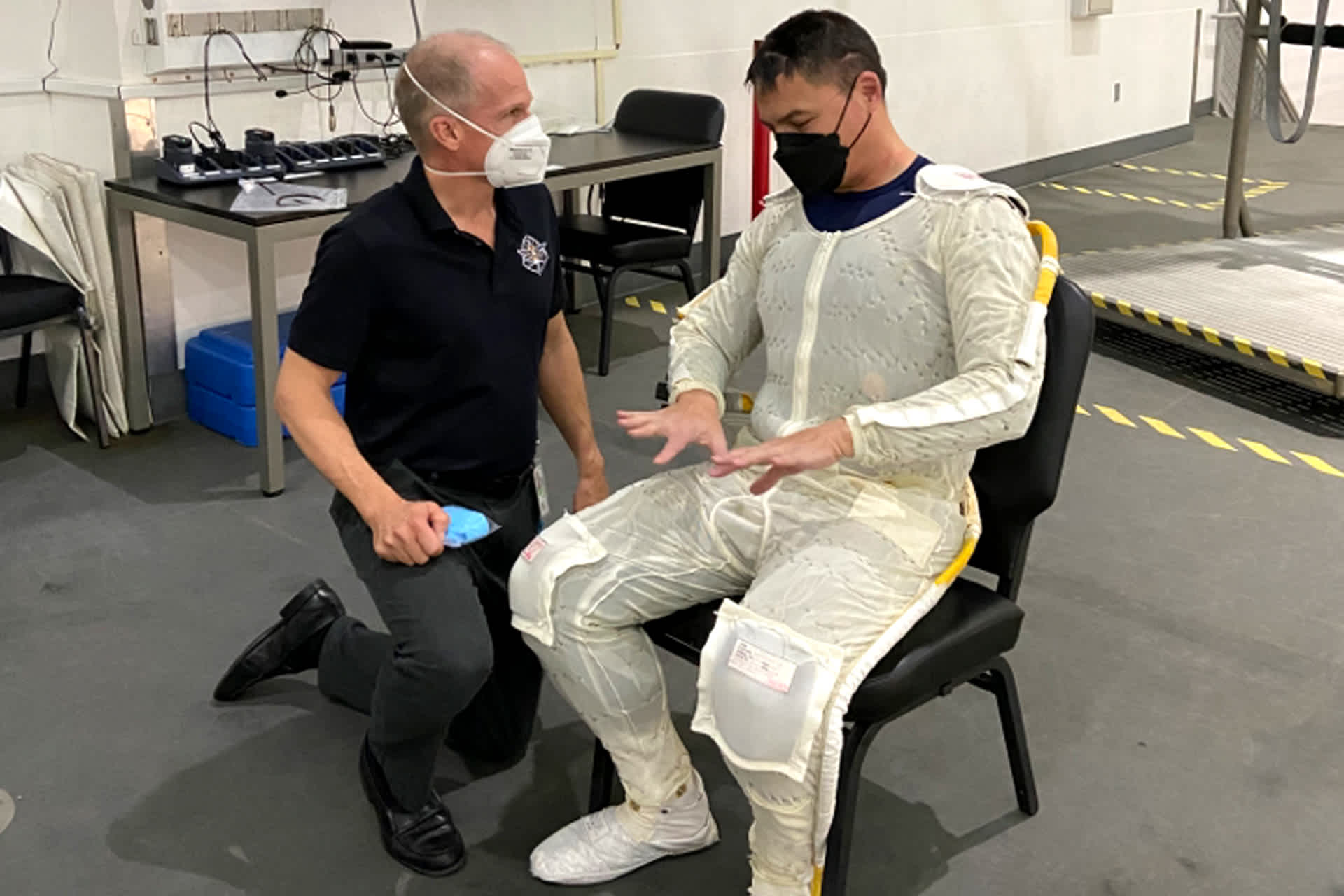 Dr. David Picken kneels next to an astronaut sitting in a chair.