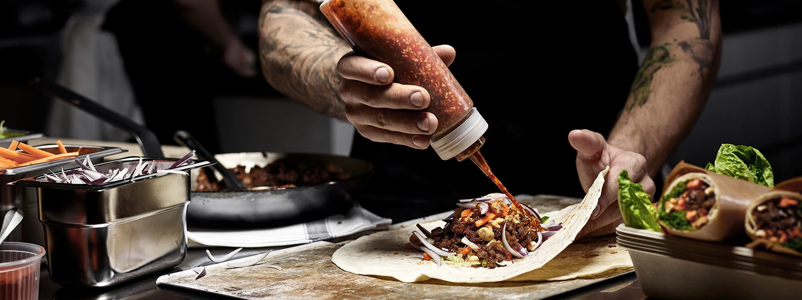 A chef putting sweet chili sauce on a loaded tortilla bread