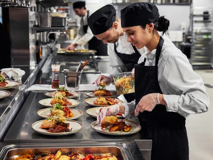 Chefs in large scale kitchen plating dishes