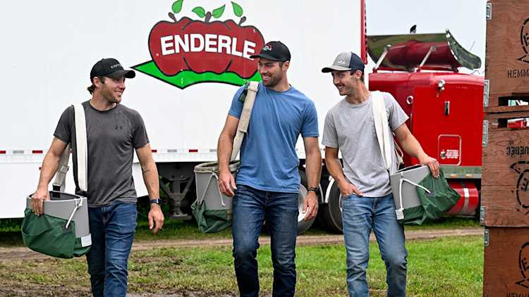 The three Enderle brothers with apple-picking bags in front of a transport truck.