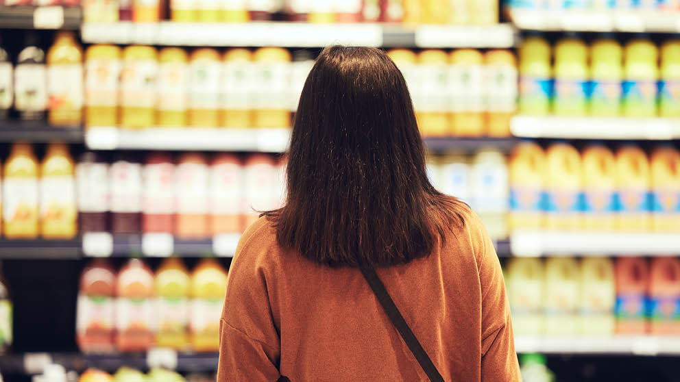 Woman looking at many options on shelf in grocery store.
