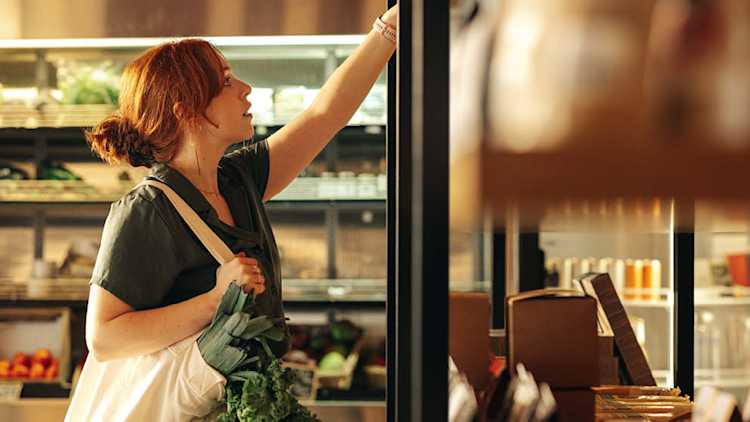 Woman in a grocery store reaches for a product in a cooler.