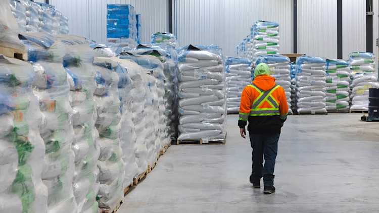Warehouse employee walking among pallets containing bags of seed.