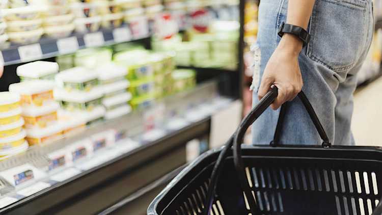 Gros plan d’une personne tenant un panier face à une étagère d’épicerie.