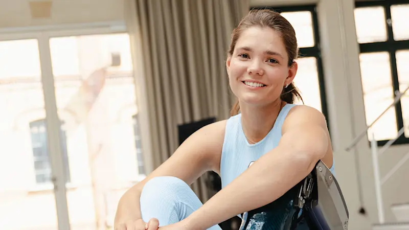 Una ragazza si riposa in palestra seduta sul suo tappetino mentre indossa l'ortesi elettronica C-Brace®