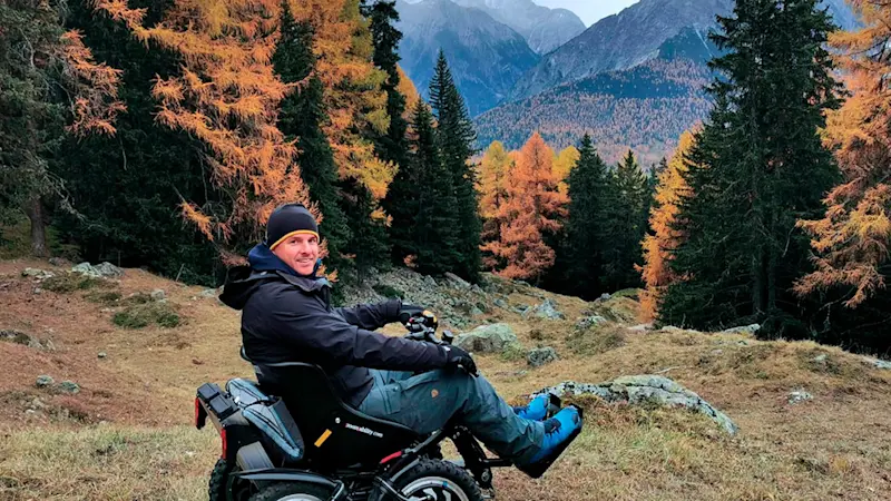 Un utente sorride a bordo del suo fuoristrada elettrico zoom davanti al panorama delle montagne