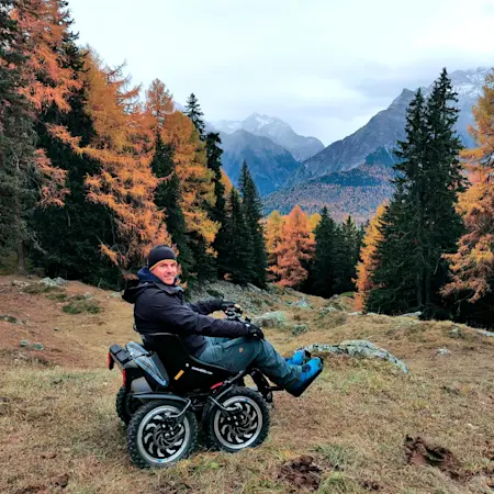 Un utente sorride a bordo del suo fuoristrada elettrico zoom davanti al panorama delle montagne