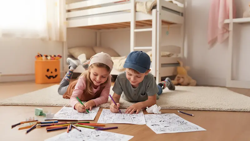 Kids filling in their Ottobock Care Halloween Coloring book together on the bedroom floor