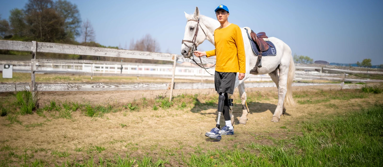 A lower limb prosthetic leg user walking outside with their horse 