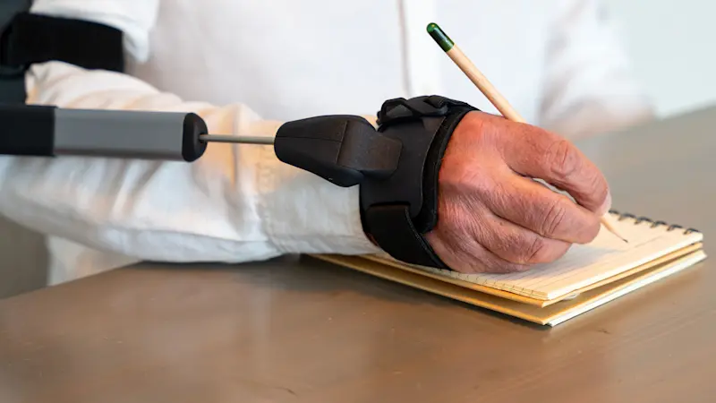 Dettaglio dell'ortesi STIL che riduce il tremore del polso di un paziente affetto da tremore essenziale mentre sta scrivendo