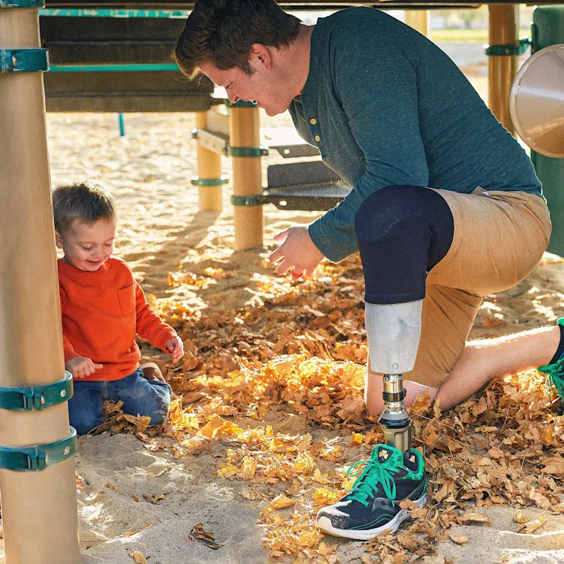 A below knee prosthesis user playing in an outdoor playground with their child