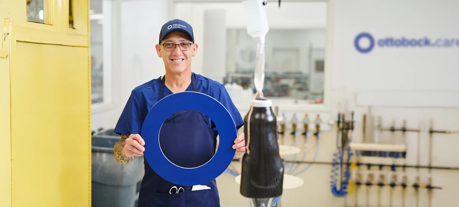 An Ottobock.care Product Technician holding the iconic O in an orthotics and prosthetics lab while smiling