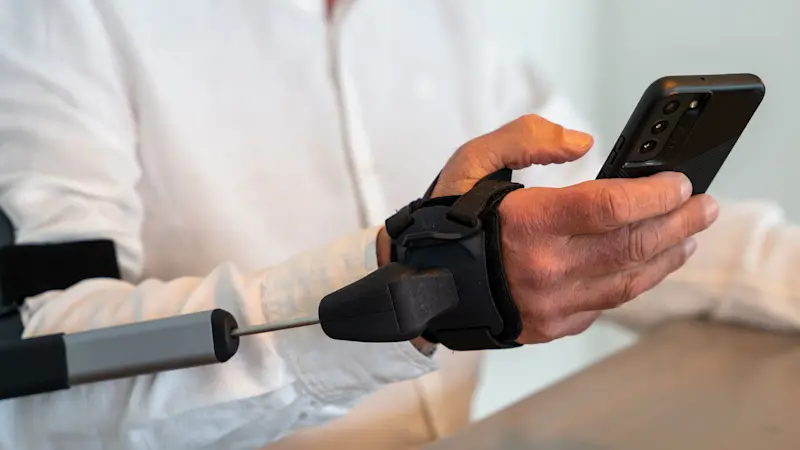 Dettaglio di un paziente che tiene in mano lo smartphone grazie all'ortesi STIL