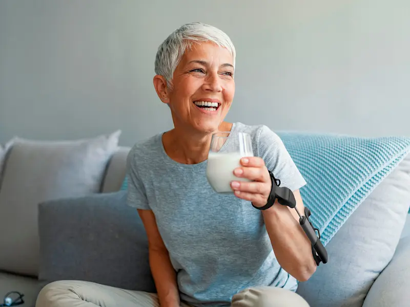 Una donna beve latte mentre indossa l'ortesi anti-tremore STIL sul suo braccio