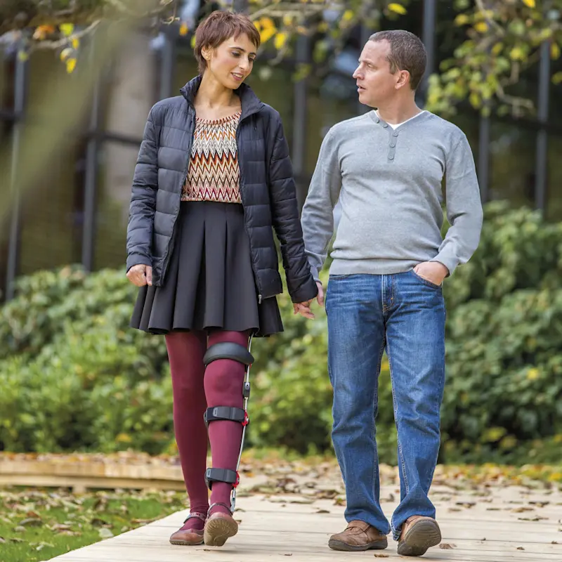 Una paziente con l'ortesi FreeWalk sulla gamba sinistra passeggia mano nella mano con il compagno
