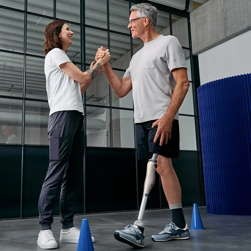 Un ortodoncista certificado golpea los cinco a un amputado por encima de la rodilla mientras practican caminar con el microprocesador de rodilla Kenevo por Ottobock