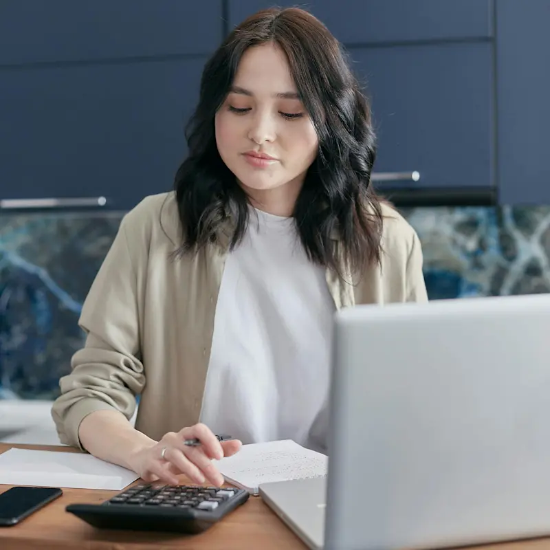 A woman using a calculator and laptop at a desk