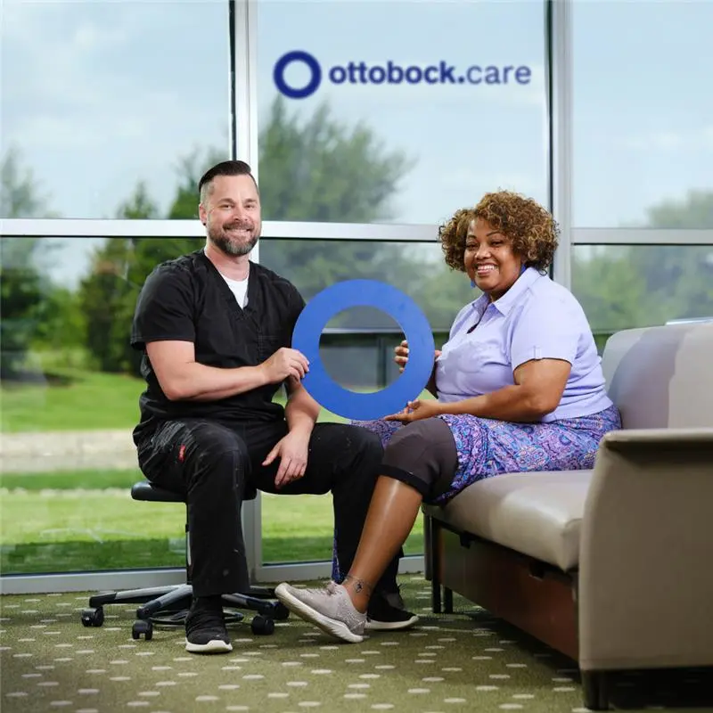 An Ottobock.care Certified Prosthetist Orthotist posing with a patient wearing a cosmetic prosthetic leg while holding the Ottobock.care O logo