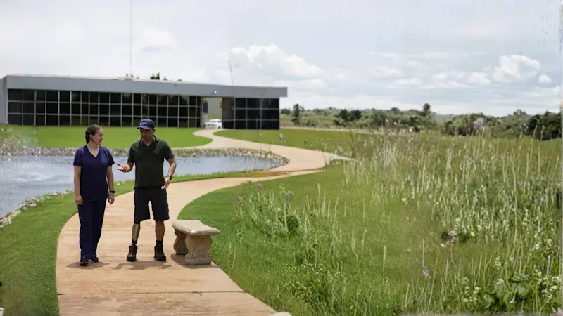 Un protésico certificado caminando por un estanque con un paciente con pérdida de extremidad
