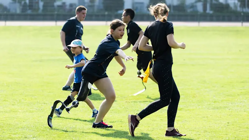 Un grupo de niños jugando al aire libre en un campo. Algunos usan cuchillas protésicas deportivas