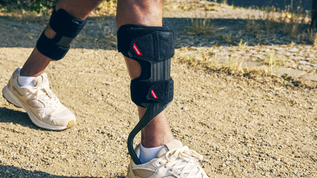 A hiker wears two Dynamic Carbon Fiber Ankle Foot Orthoses while walking on a trail