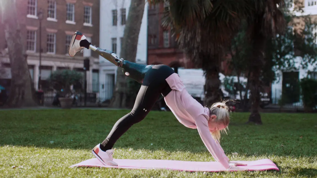 Un usuario de pie protésico practicando yoga en un parque