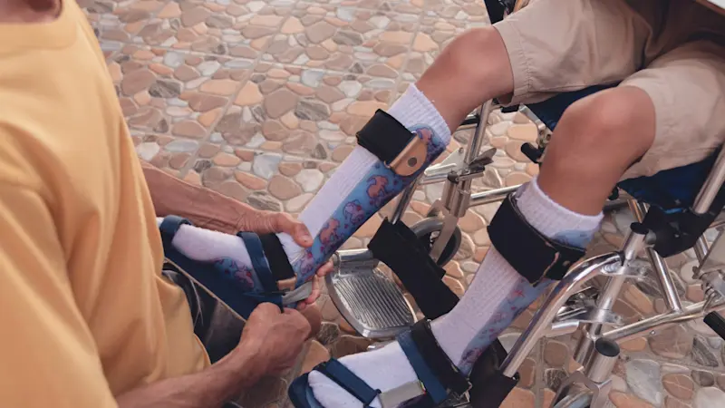 A patient in a wheelchair being assisted adjusting their solid ankle foot orthosis