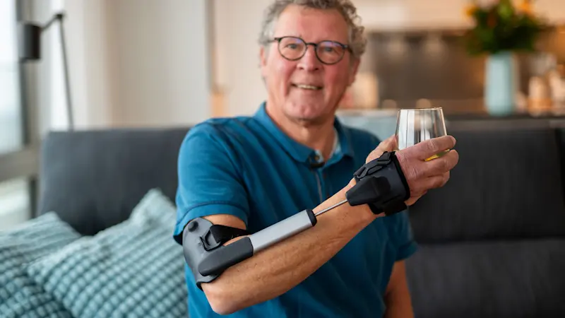 Un uomo tiene sollevato in aria un bicchiere mentre indossa l'ortesi STIL sull'avambraccio