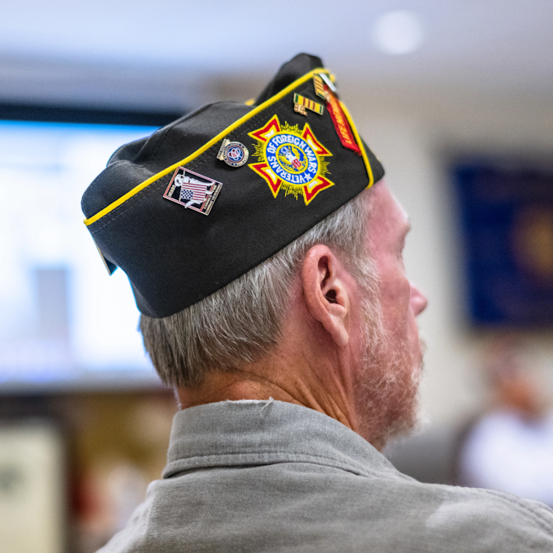 A veteran wearing a decorated hat showcasing various accolades and accomplishments