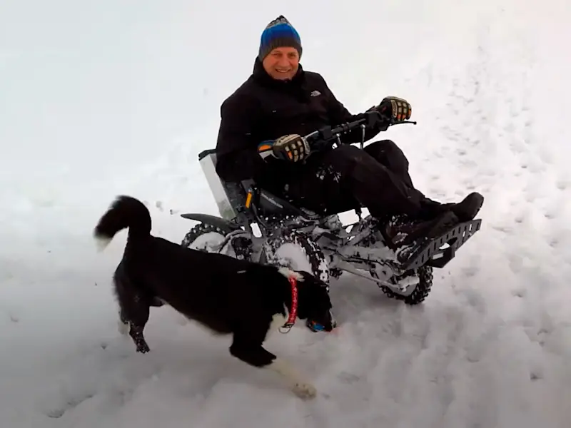 Un uomo a bordo del fuoristrada elettrico Zoom sulla neve insieme al suo cane