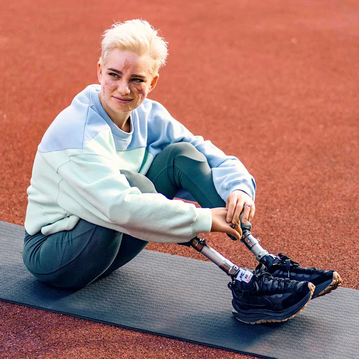 El usuario de pierna protésica Ottobock, Bebe, se sienta en una esterilla de yoga en un gimnasio al aire libre