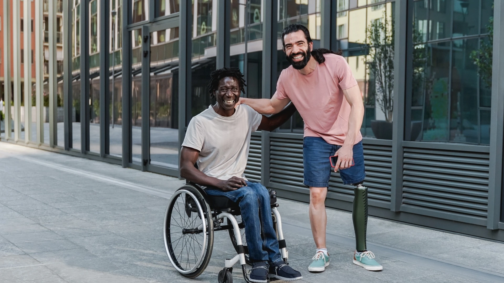 Two people living with limb difference posing for a photo on a public street