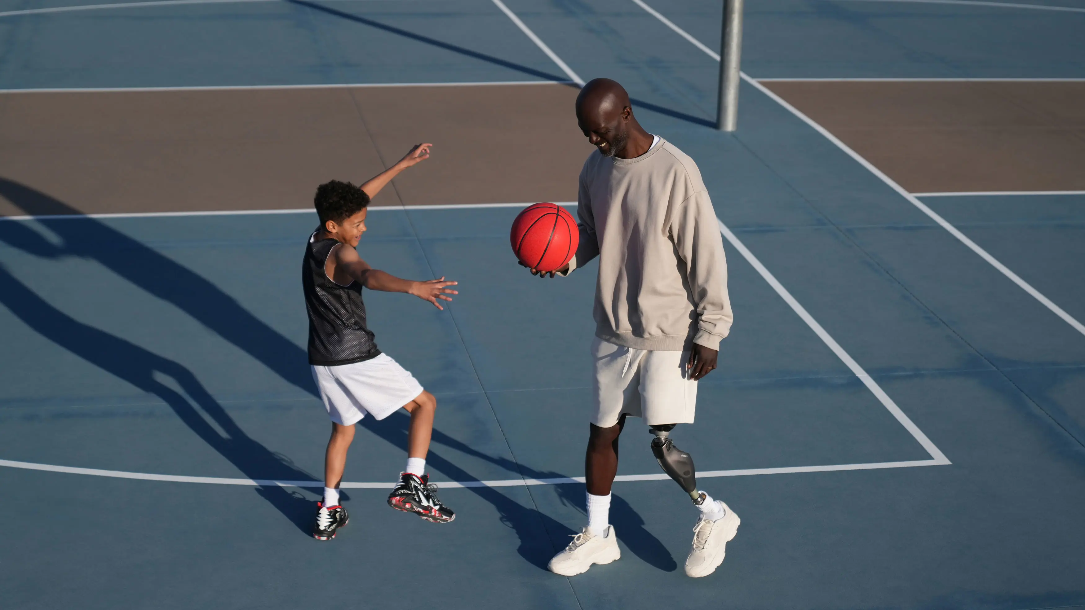 A father wearing the Kenevo by Ottobock and son playing basketball on an outdoor court