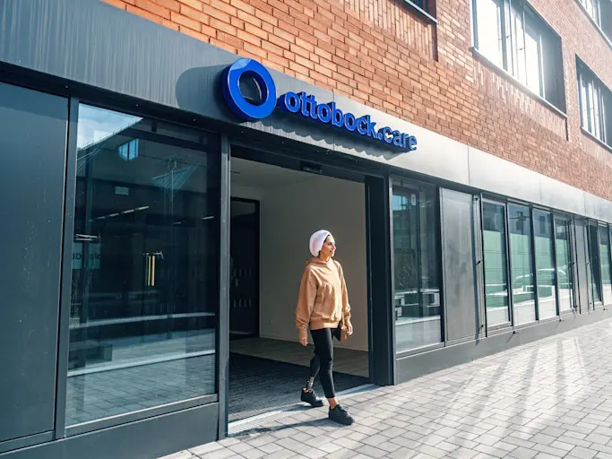 An amputee patient walking out of an Ottobock.care clinic location with a brick exterior