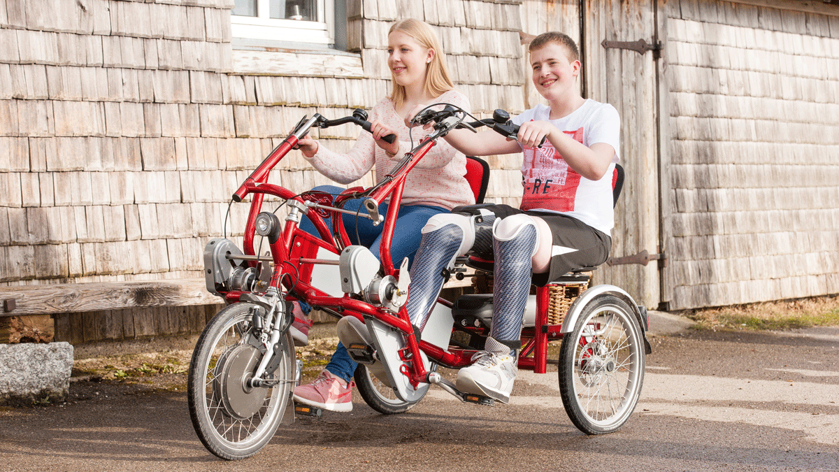 A young man and woman pedaling on a side-by-side trike. One is wearing a knee-ankle-foot orthotic brace
