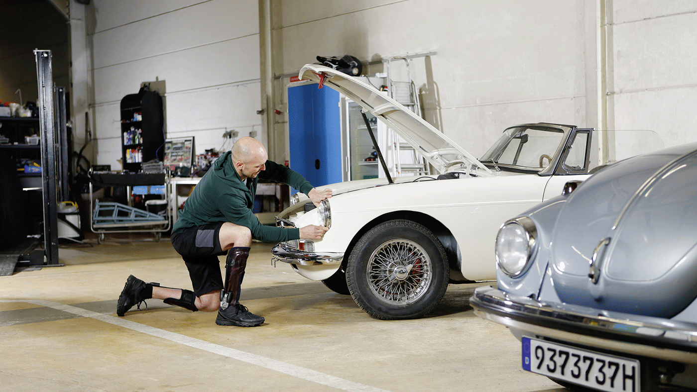 A man in a knee-ankle-foot orthosis crouching in front of a car to replace the headlights