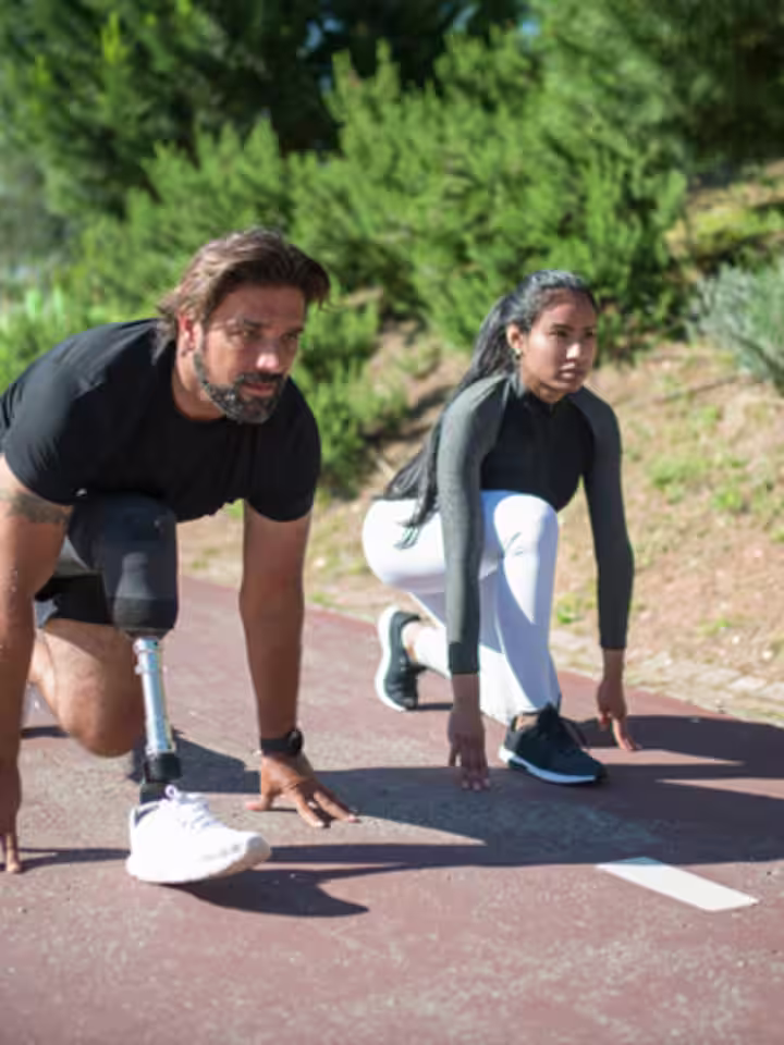 Un usuario atlético de pierna protésica en posición de cuclillas antes de comenzar su carrera en una pista de carreras al aire libre