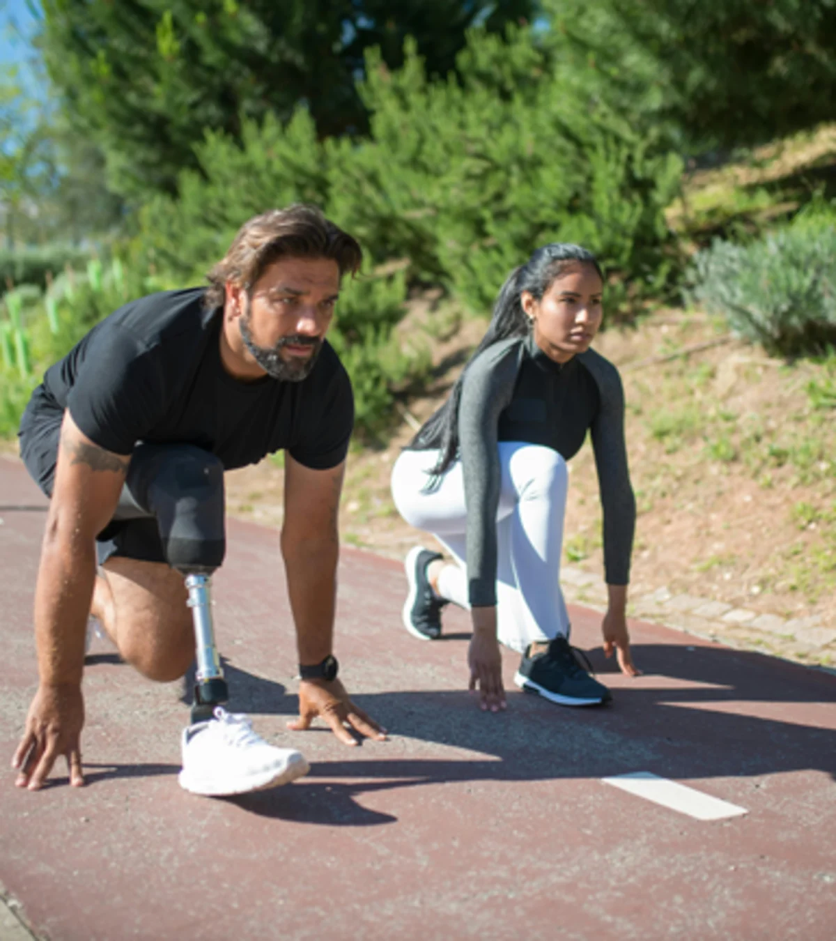 Un usuario atlético de pierna protésica en posición de cuclillas antes de comenzar su carrera en una pista de carreras al aire libre