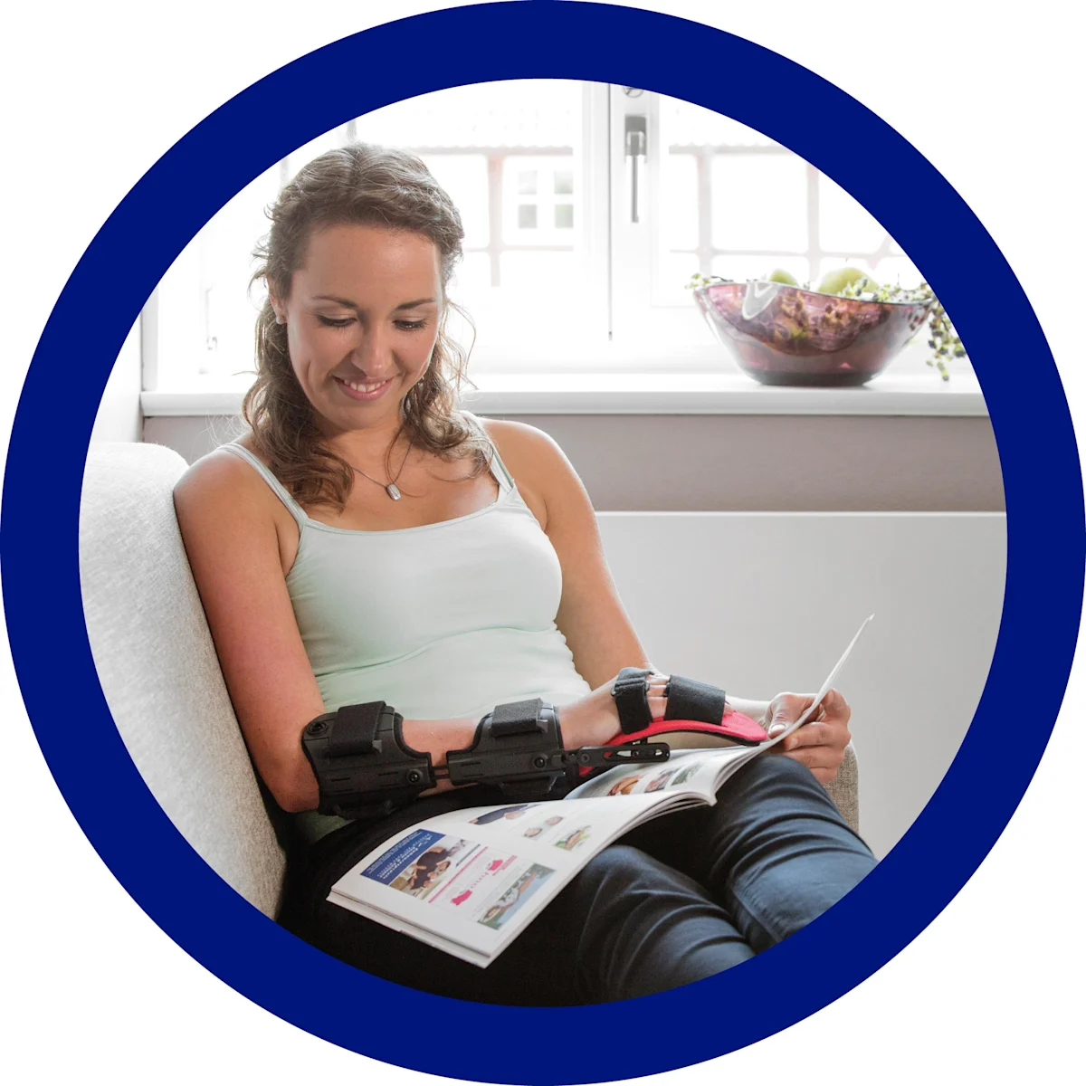 Una ragazza con l'ortesi neurologica di polso Manu Neurexa Plus sfoglia una rivista seduta sul divano