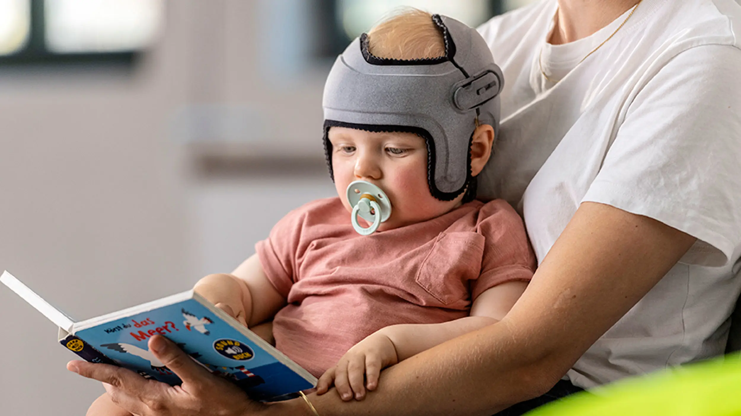 An infant wearing the custom MyCRO Band cranial helmet for children while their parent reads them a book