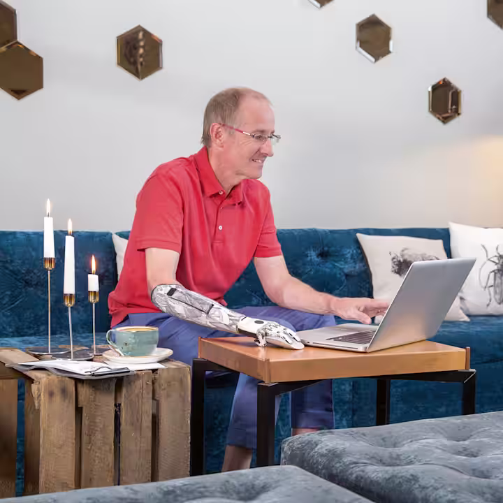 A prosthetic arm user browsing on their laptop in their living room