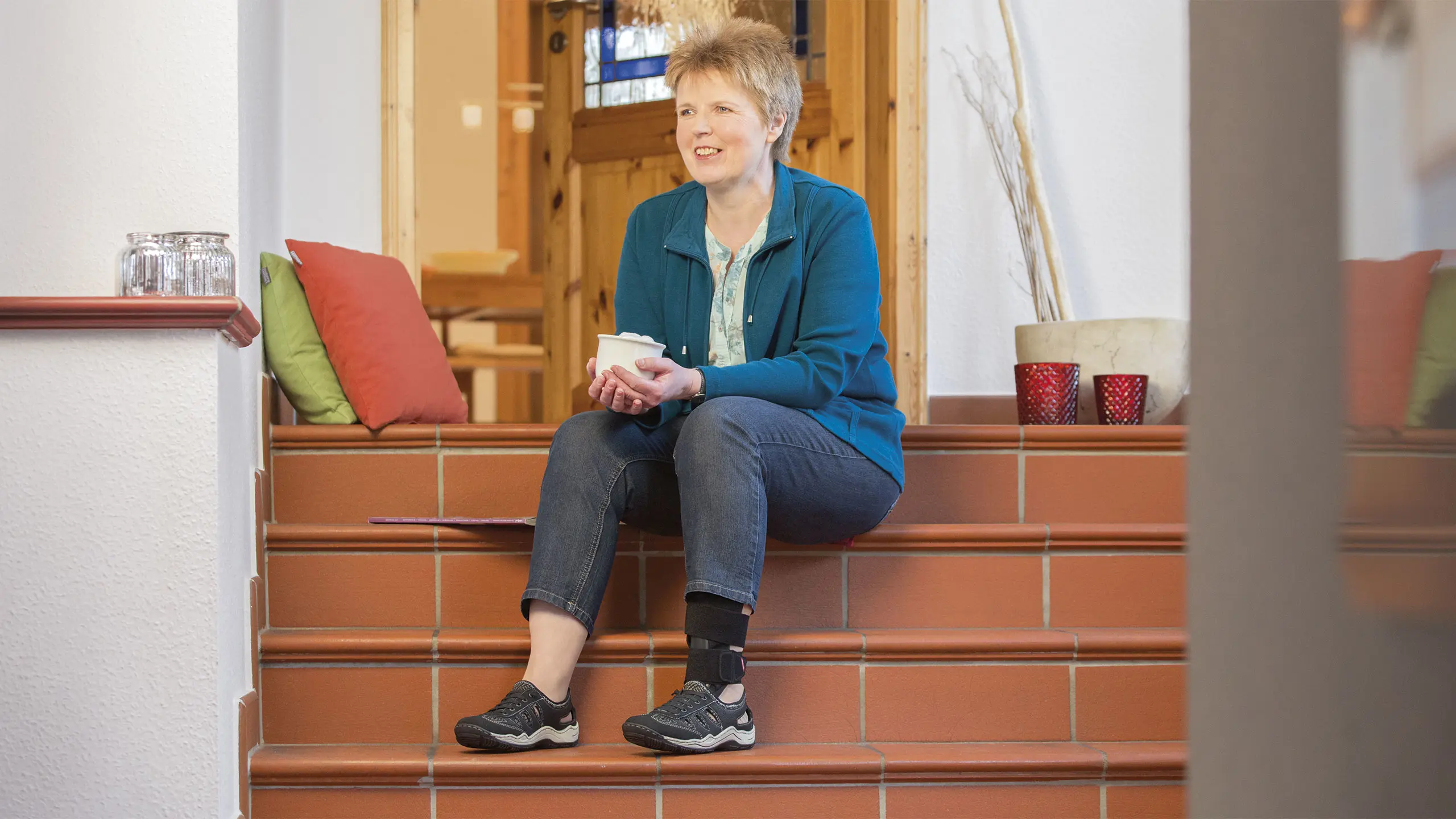 Una paziente con l'ortesi neurologica GoOn nella caviglia sinistra si rilassa seduta sulle scale di casa