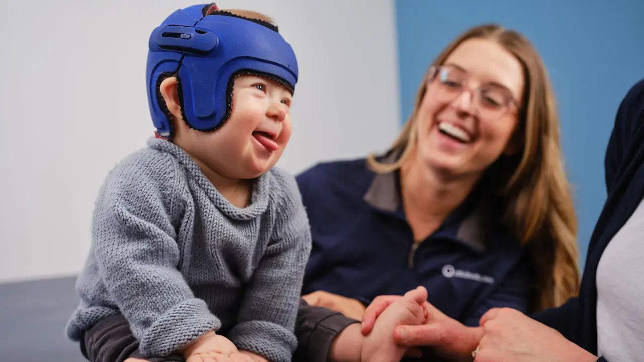 A pediatric patient wearing a cranial orthosis helmet laughing