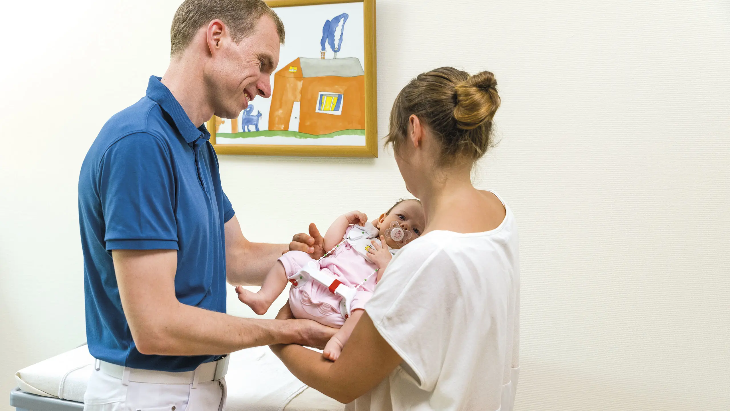 Due genitori stringono in braccio il loro bambino con l'ortesi di flessione e abduzione d'anca Tübingen
